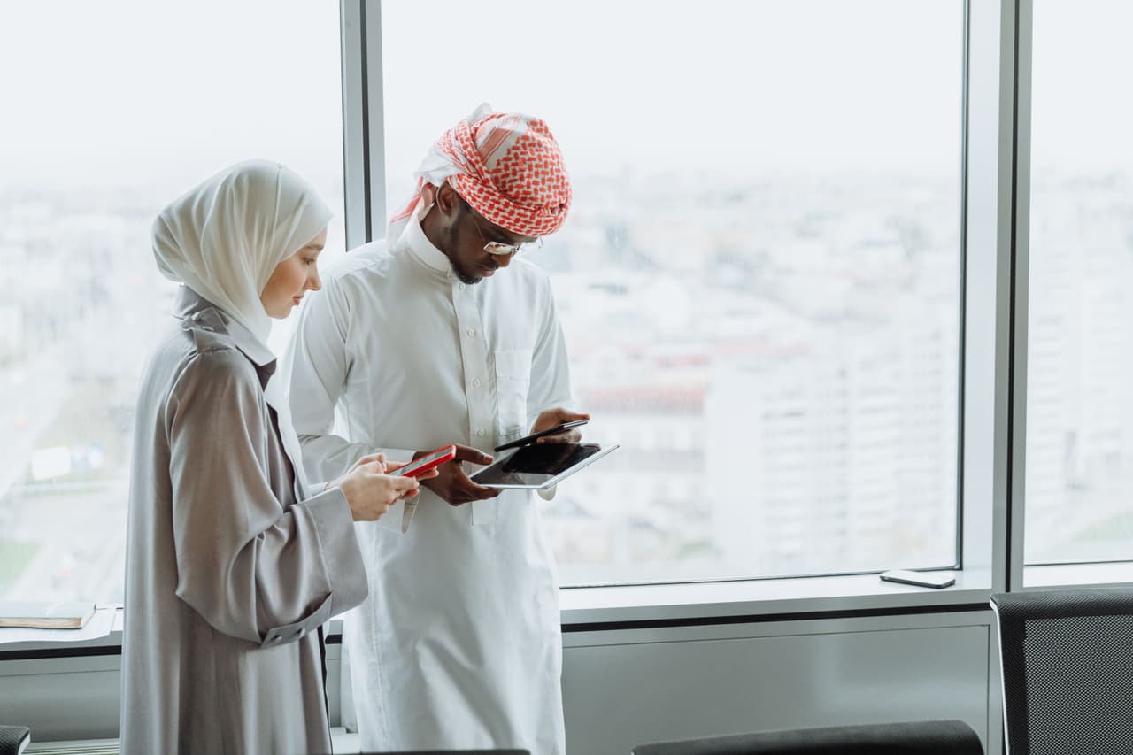 زميلان يقفان بجوار نافذة مكتب، أحدهما يستخدم هاتفًا والآخر جهازًا لوحيًا